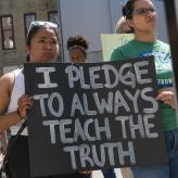 Woman holding sign that reads "I pledge to always teach the truth"