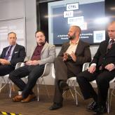 A white woman and four men sitting in chairs in straight line. Behind them a board says "Ctrl Alt Delete Hate".