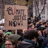 Protesters, and one protesters holding a board that reads "climate justice now!"