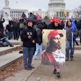 A woman wearing a Make America Great Again cap carrying an image of Jesus wearing a MAGA hat with "WWG1WGA" on his lapel