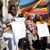 A woman in the front of the frame holding a sign that reads "marching in solidarity with the Ugandan LGBTI Community"